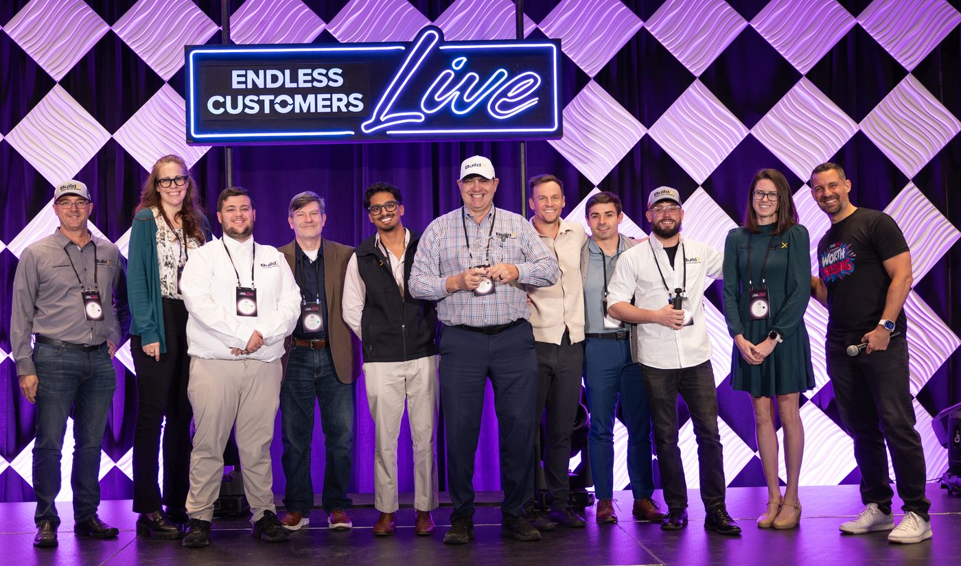 Buz Artiano holding the Fearless Content Award on stage at Endless Customers Live with the BuildX team and IMPACT hosts